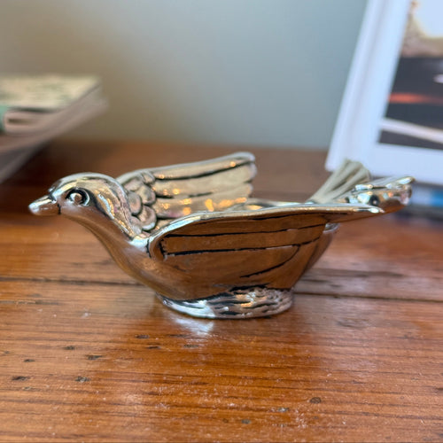 Silver bird-shaped object on a wooden surface with a blurred background